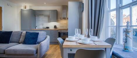 Una cocina moderna con armarios grises, una mesa de comedor preparada para cuatro personas y vistas de la ciudad a través de amplios ventanales.