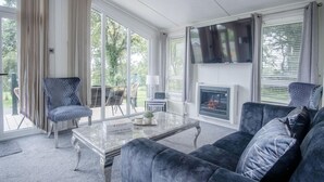 A spacious living room with a large window, a fireplace, and a television. - 1 Manor Lodge - 3 Bedroom Lodge - Pendine (Carmarthen)