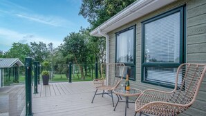 A wooden deck with wicker chairs and a bottle of champagne, overlooking a green landscape. - 1 Manor Lodge - 3 Bedroom Lodge - Pendine (Carmarthen)