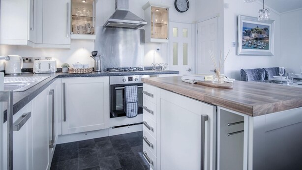 A modern kitchen with white cabinetry, a stainless steel range hood, and a wooden countertop. - 1 Manor Lodge - 3 Bedroom Lodge - Pendine (Carmarthen)