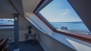 A room with a skylight, a small table with a plant, and a view of the sea and buildings.