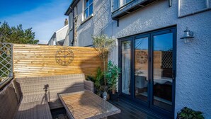 A patio with wicker furniture, a wooden wall with a clock, and a glass door leading to a covered area.