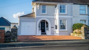 A two-story house with a white facade, a central entrance with a black door, and a brick driveway.