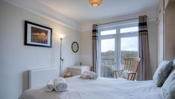 A hotel room with a large bed, a chair by the window, a framed picture on the wall, and a view of the outdoors.