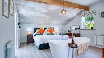 A bedroom with a large bed, a bathtub, and a window with a view of greenery.