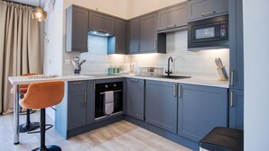 A modern kitchen with grey cabinets, a built-in microwave, and a stainless steel sink. - The Pig Sty - 1 Bedroom Studio - Princes Gate (Narberth)