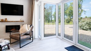 A modern living room with a fireplace, a comfortable chair, and a large TV mounted on the wall. - The Pig Sty - 1 Bedroom Studio - Princes Gate (Narberth)