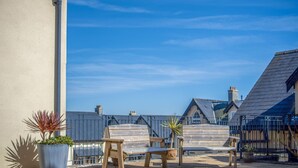 A rooftop patio with wooden benches and potted plants, overlooking a residential area with pitched roofs. - 29 Rhodewood House - 2 Bedroom - Saundersfoot (Saundersfoot)