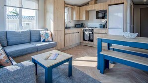 Una cocina moderna con armarios de madera, horno empotrado y microondas. Hay un sofá azul y una pequeña mesa con una revista.