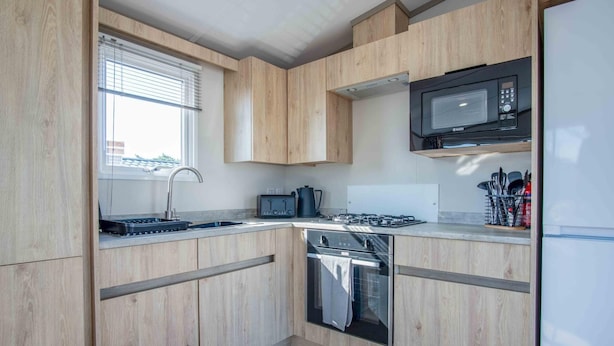 Una cocina moderna con armarios de madera, microondas integrado, estufa a gas y lavavajillas.