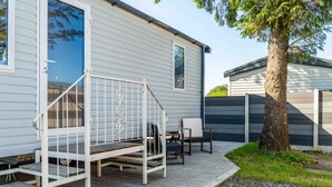 Una casa móvil con un patio, que incluye una escalera metálica, mobiliario exterior y un árbol.