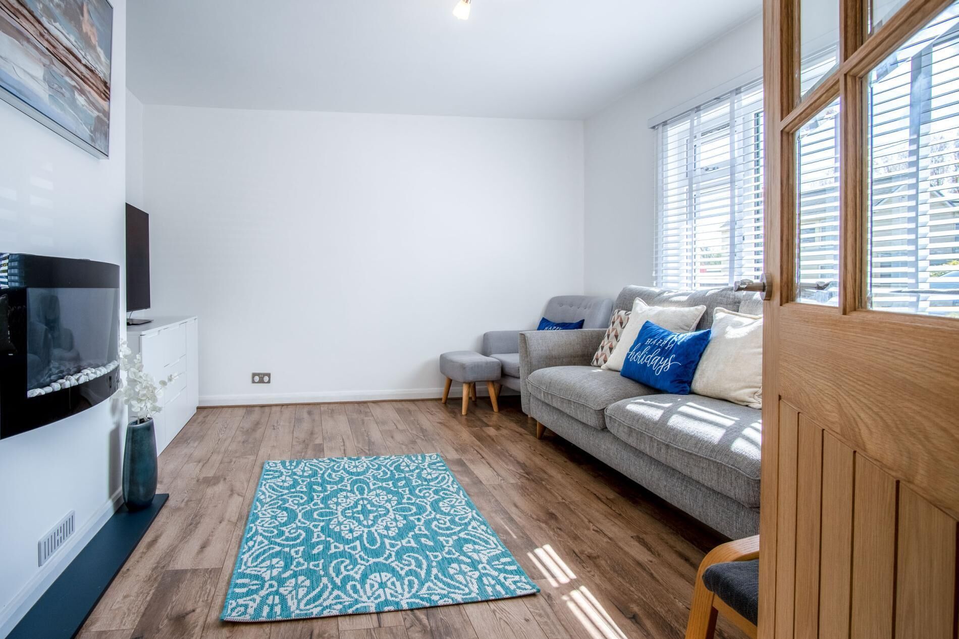 A modern living room with a grey sofa, a blue patterned rug, and a flat-screen TV.