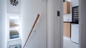 A hallway with a wooden bat leaning against the wall, a fire exit sign, and a kitchen area with cabinets and a refrigerator.