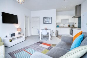 A modern living room with a grey sofa, colorful rug, and a flat-screen TV mounted on the wall. - Bay View - 2 Bedroom Apartment - Tenby (Tenby)