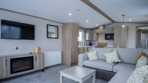A modern living room with a grey sofa, a white coffee table, a fireplace, and a kitchen area with a microwave and a TV.
