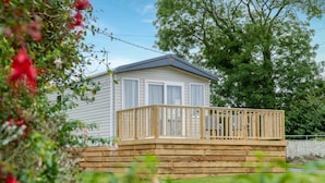 A single-story mobile home with a wooden deck and a fenced yard.