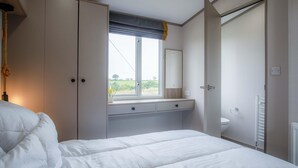 A bedroom with a bed, a window with a view of greenery, a wardrobe, and a bathroom with a toilet and a towel rack.