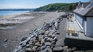 Une plage rocheuse avec un mur de pierres et un bâtiment doté d’un balcon donnant sur la mer.