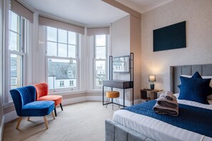 A hotel room with a bed, a desk, a chair, and large windows. - The Lanterns - 9 Bedroom - Sleeps 17 - Saundersfoot Village Centre (Saundersfoot)