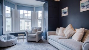 A room with a bay window, a grey armchair, a sofa with plaid cushions, and a bean bag chair. - The Lanterns - 9 Bedroom - Sleeps 17 - Saundersfoot Village Centre (Saundersfoot)