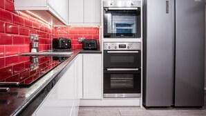 A kitchen with a red tiled backsplash, stainless steel appliances, and a double oven. - The Lanterns - 9 Bedroom - Sleeps 17 - Saundersfoot Village Centre (Saundersfoot)