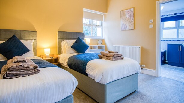 A hotel room with two beds, a view of the outside, and a bathroom visible through an open door. - The Lanterns - 9 Bedroom - Sleeps 17 - Saundersfoot Village Centre (Saundersfoot)