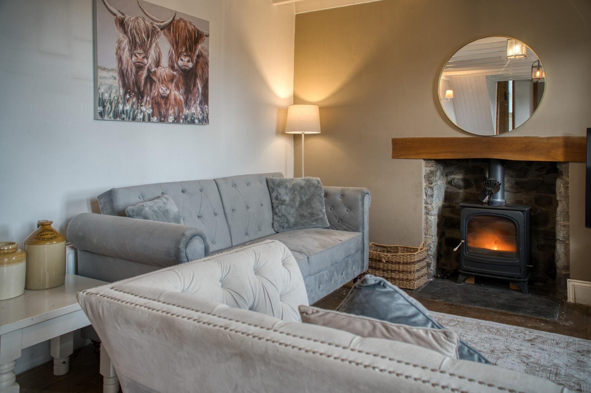 A cozy living room with a grey sofa, a white armchair, a fireplace, and a painting of animals.