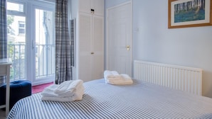 Une chambre avec une couvre-lit à rayures, une fenêtre avec des rideaux, un radiateur et un tableau encadré au mur.