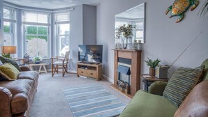Un salon avec un canapé en cuir marron, un meuble TV en bois, une cheminée et une grande fenêtre avec des stores.
