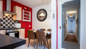 Une cuisine moderne avec des murs rouges, un pare-feu à carreaux noirs et blancs, et un coin repas agrémenté d’une horloge ronde.