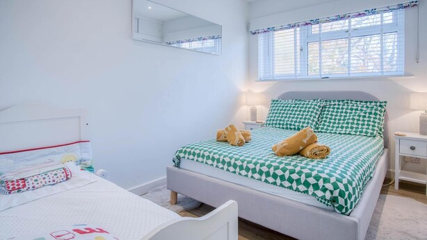 Een slaapkamer met een bed, nachtkastjes, een bureau, een spiegel en een raam met zonwering.