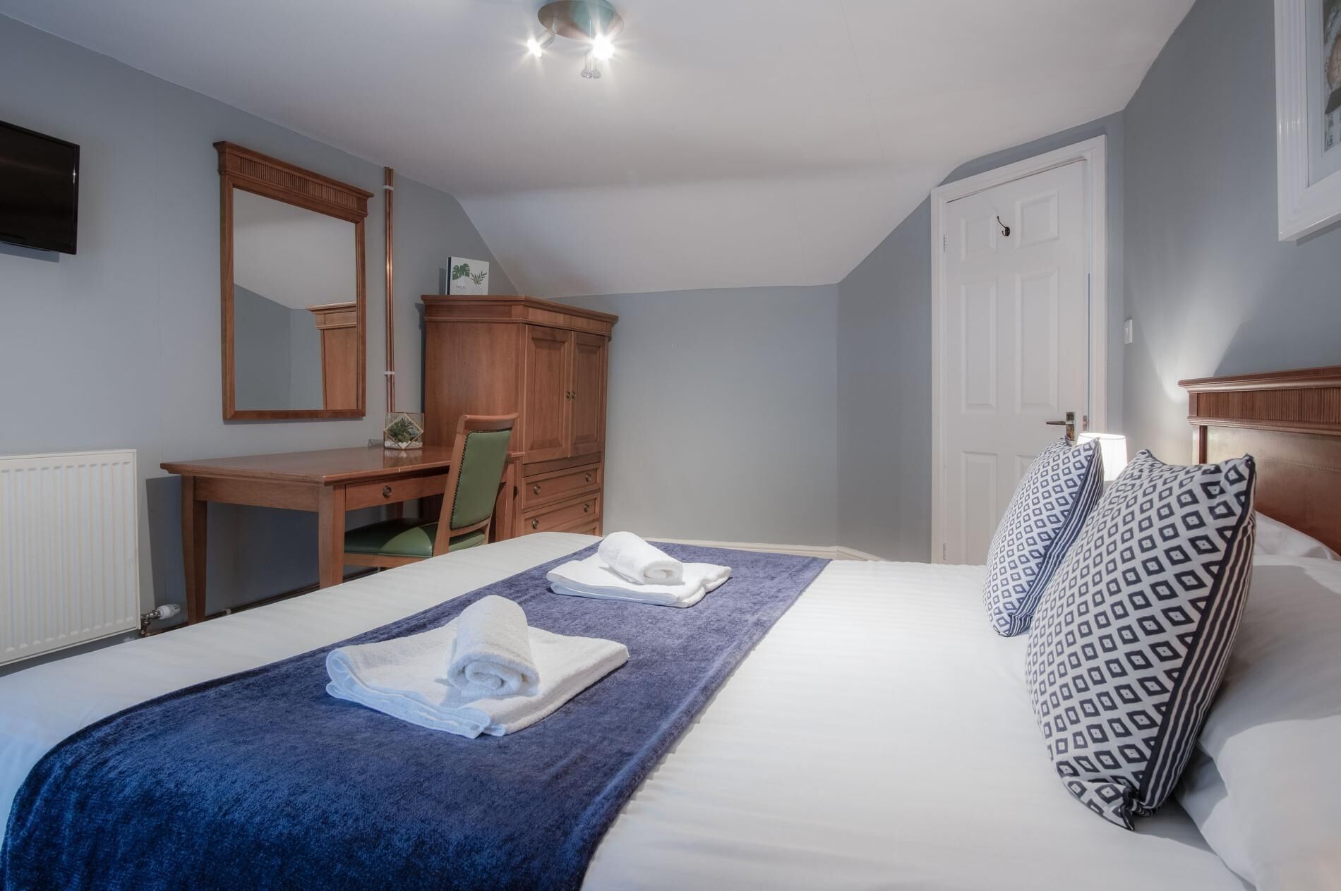 A bedroom with a bed, a desk, a chair, a wardrobe, and a mirror.
