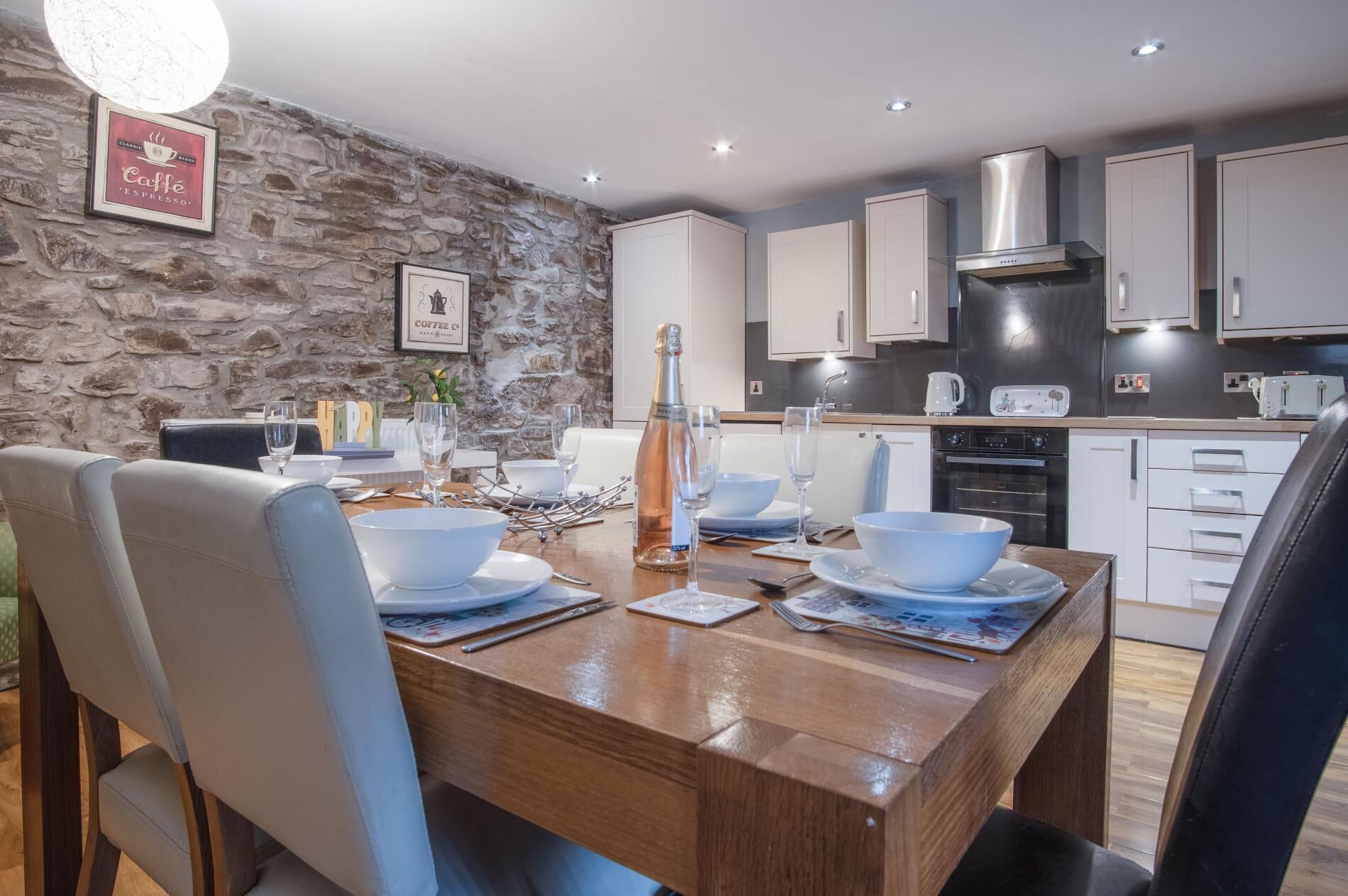 Una cocina moderna con pared de piedra, mesa de comedor de madera y armarios blancos.