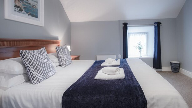Una cama bien hecha con almohadillas estampadas, una manta azul y una toalla blanca.