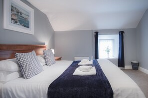 A neatly made bed with patterned pillows, a blue throw blanket, and a white towel. - Fletcher Coach House - 3 Bedroom Cottage - Pendine (Carmarthen)