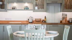 A modern kitchen with light grey cabinets, a wooden countertop, and a dining table set with white plates and glasses. - 3 St Bride s Bay View - 3 Bedroom - Broad Haven (Haverfordwest)