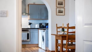 A kitchen with a washing machine, a coffee maker, and a dining table with a bottle of wine. - Marina House Annex - 1 Bedroom - Neyland (Milford Haven)
