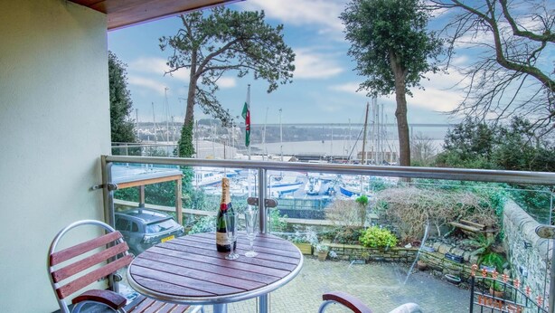 A balcony with a table and chairs, overlooking a marina with boats. - Marina House Annex - 1 Bedroom - Neyland (Milford Haven)