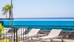 Un espace aménagé au bord de la piscine, avec des chaises longues et une vue dégagée sur l’océan.