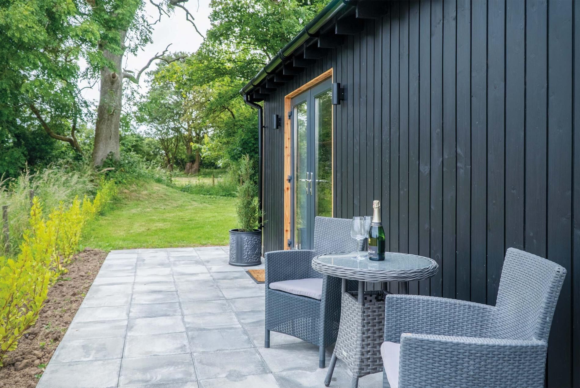 An outdoor patio with wicker furniture and a table, a bottle of champagne, and a potted plant.