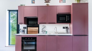 Una cocina moderna con armarios rosados, un horno negro, un microondas y una tabla de cortar de madera.
