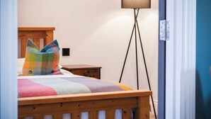Un dormitorio con una cama de madera, almohadas coloridas, una mesita de noche y una lámpara de pie.