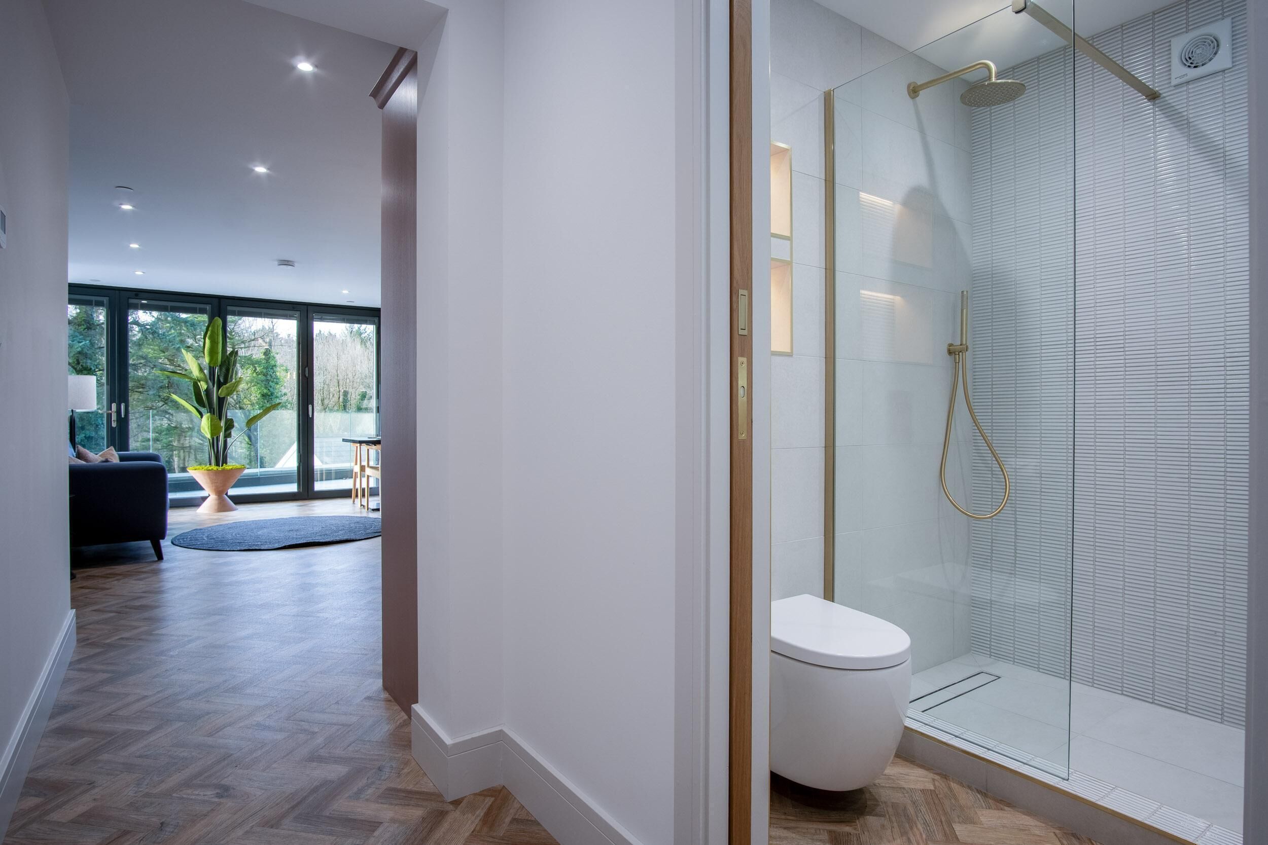 A modern bathroom with a glass shower enclosure, a white toilet, and a wooden floor.