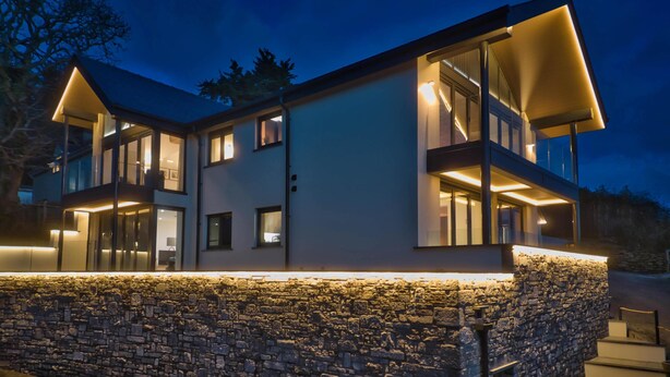 Une maison moderne à deux étages, avec des fondations en pierre, de grandes fenêtres et un balcon.