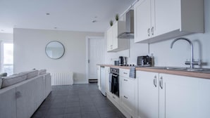 A modern kitchen with white cabinets, a built-in oven, and a sink. - Ridgeway Retreat - 1 Bedroom Cottage - Manorbier (Tenby)