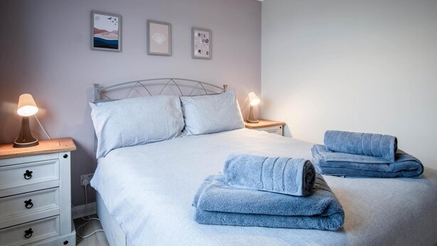 A neatly made bed with two pillows, a bedside table with a lamp, and a wall with three framed pictures. - Swanbrook - 2 Bedroom Chalet- Freshwater East (Pembroke)