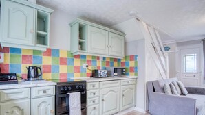 A kitchen with light green cabinets, a colorful tile backsplash, a stove, a microwave, and a toaster. There is a gray sofa with pillows in the corner. - Swanbrook - 2 Bedroom Chalet- Freshwater East (Pembroke)