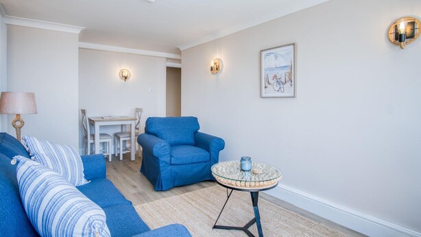 Ein Wohnzimmer mit einem blauen Sofa, einem kleinen runden Tisch und einem Essbereich mit weißem Tisch und Stühlen.