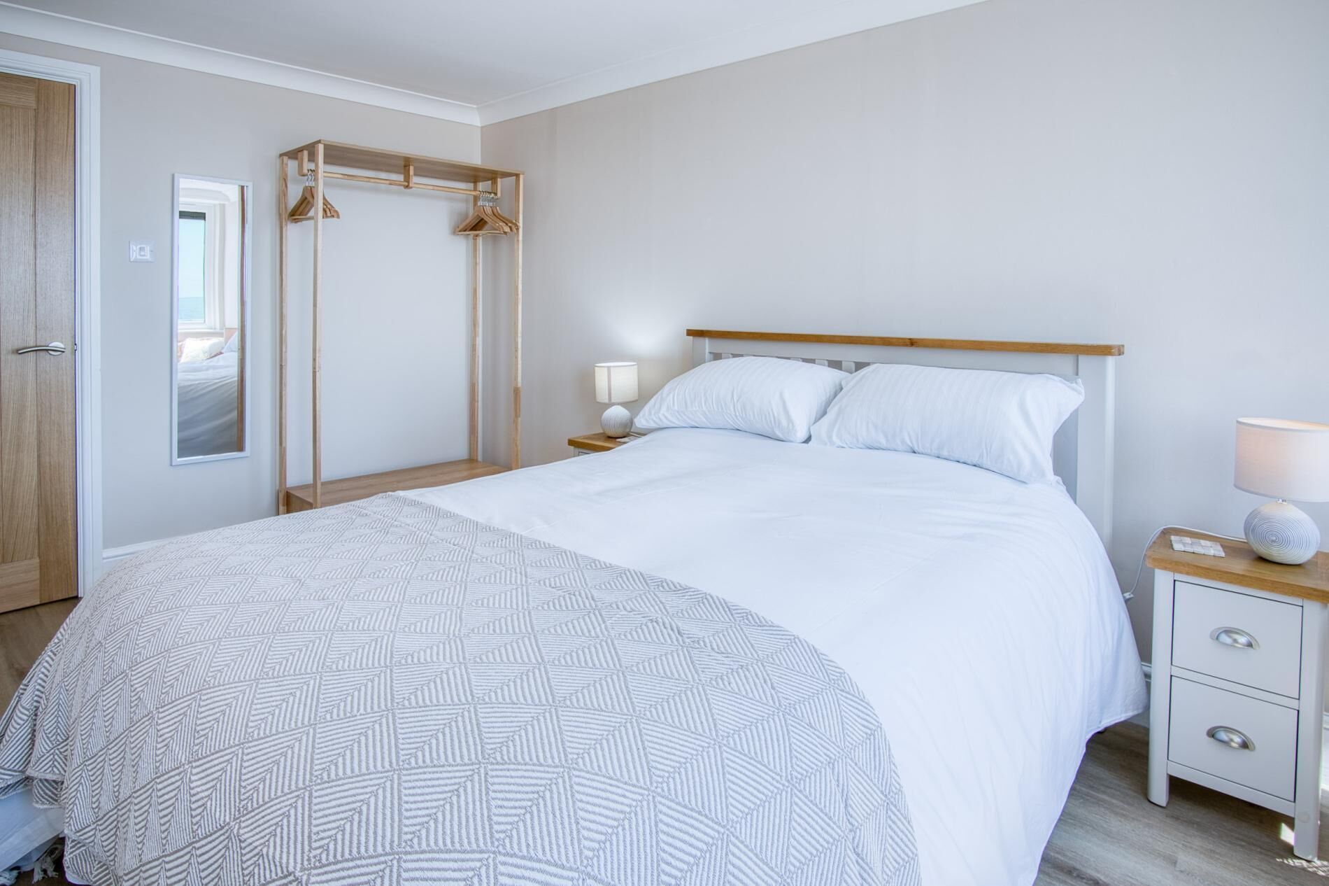 Une chambre bien rangée, avec un lit, des tables de chevet, un miroir et une armoire en bois.