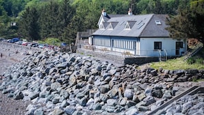 Ein Küstengebäude mit Steinfundament, geneigtem Dach und einem kleinen Balkon.